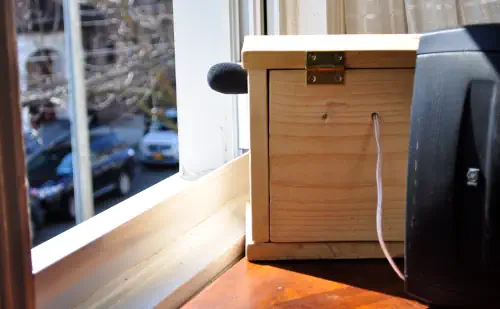 A wooden box with a microphone pointing out a summertime window